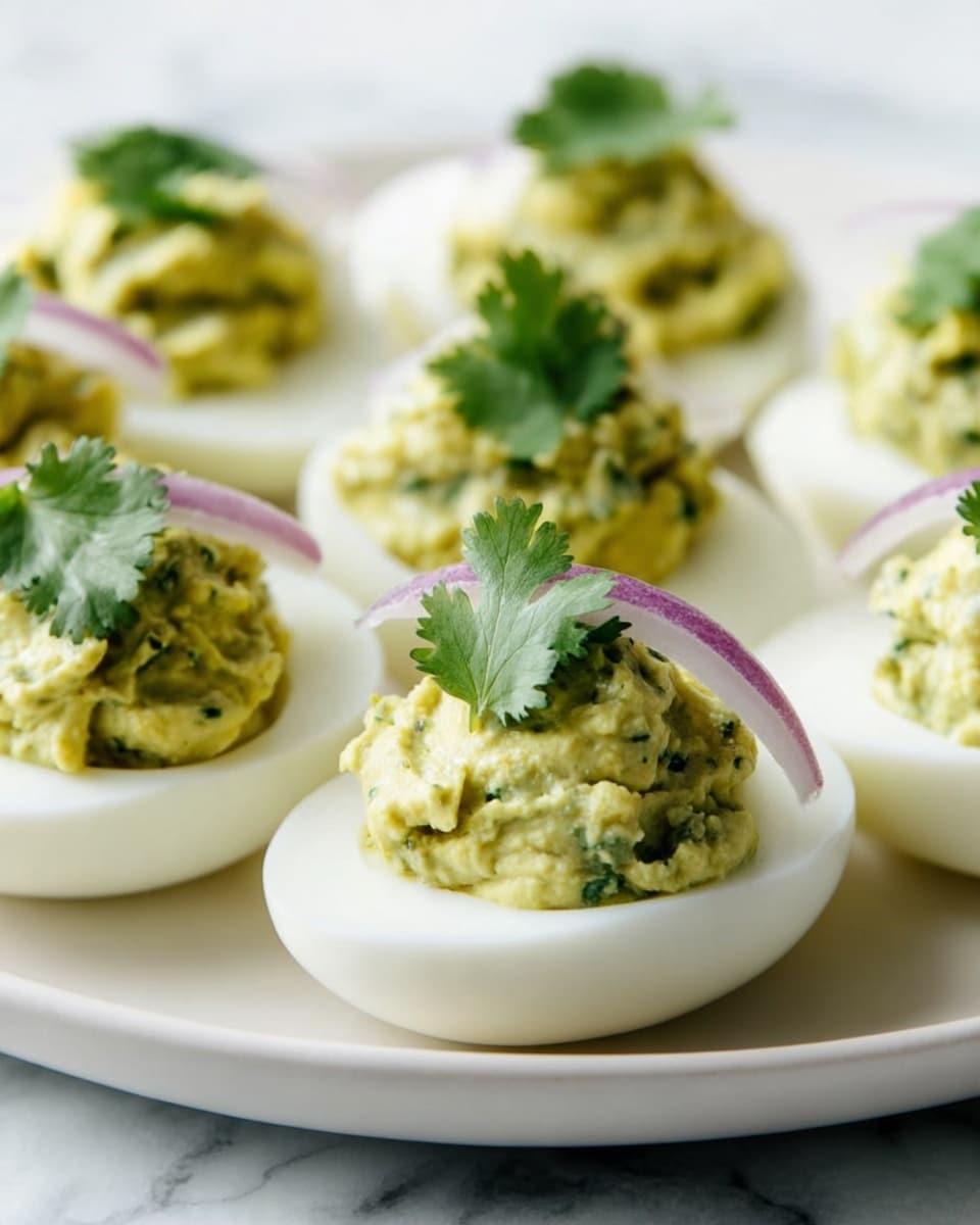 The image shows a white plate with several deviled eggs neatly arranged. Each egg half has a smooth white base layer with a thick layer of creamy, greenish-yellow filling on top that looks slightly chunky with specks of green herbs inside. The filling is topped with a small piece of dark green cilantro leaf and a thin slice of light purple onion. The plate sits on a white marbled surface. Photo taken with an iphone --ar 4:5 --v 7
