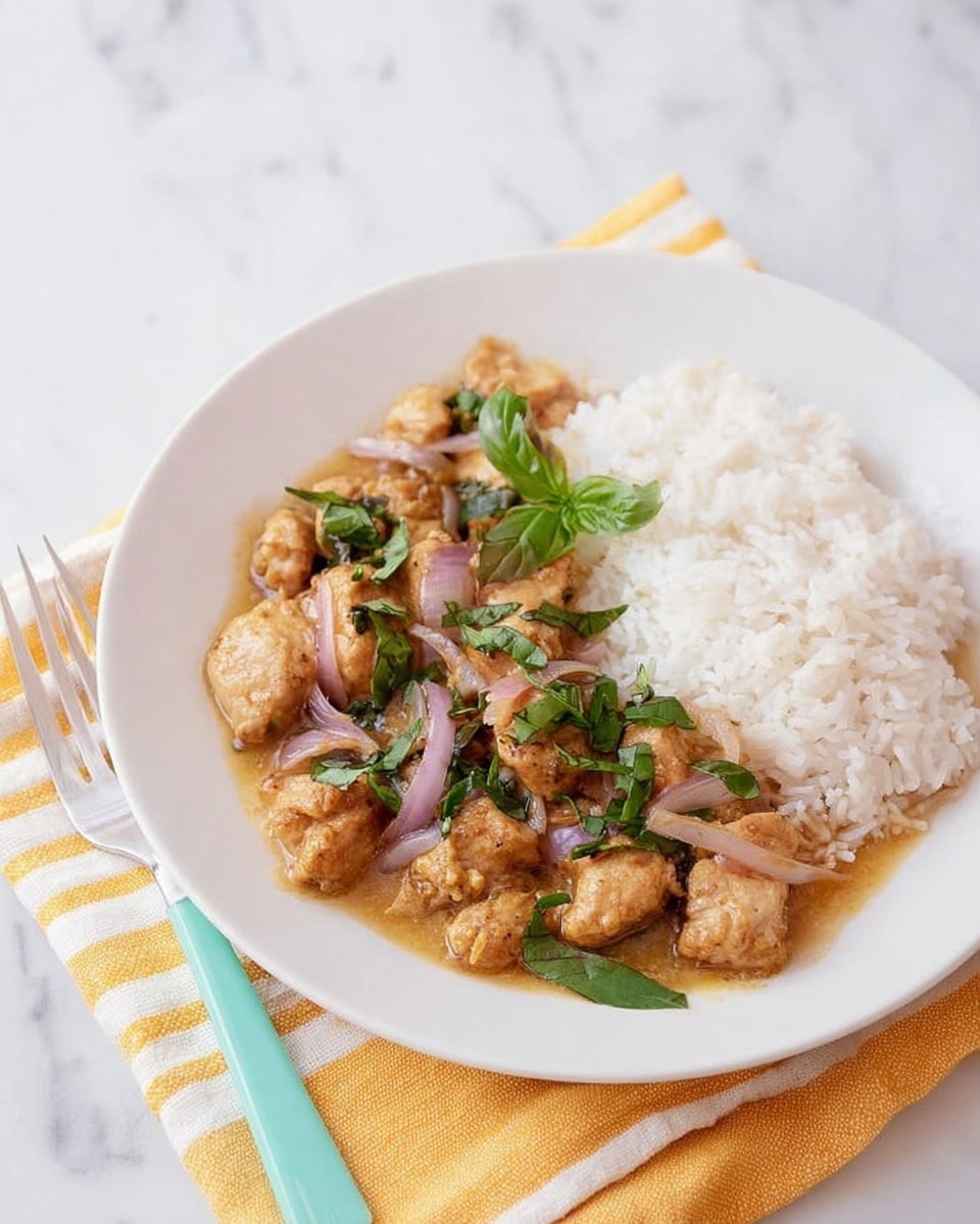 A white round plate holds a meal with two main parts: on the right side, there is a mound of plain white rice with a soft, fluffy texture. On the left side, golden brown pieces of seasoned cooked chicken sit in a light brown sauce mixed with slightly translucent cooked red onion slices and fresh green basil leaves scattered on top. The plate rests on a yellow and white striped cloth, placed on a white marbled surface. A fork with a turquoise handle lies next to the plate. photo taken with an iphone --ar 4:5 --v 7