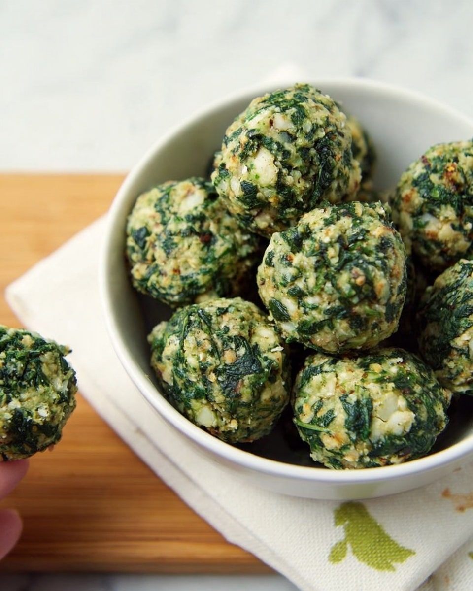 The image shows a white bowl filled with round green and beige balls that look like spinach and bread mixture. The balls have a rough texture with visible bits of green leafy pieces and soft beige chunks. The bowl is placed on a wooden board with a white napkin that has some green leaf designs. There is part of a woman's hand holding one of these balls at the lower left corner of the image. The background surface is a white marbled texture. photo taken with an iphone --ar 4:5 --v 7