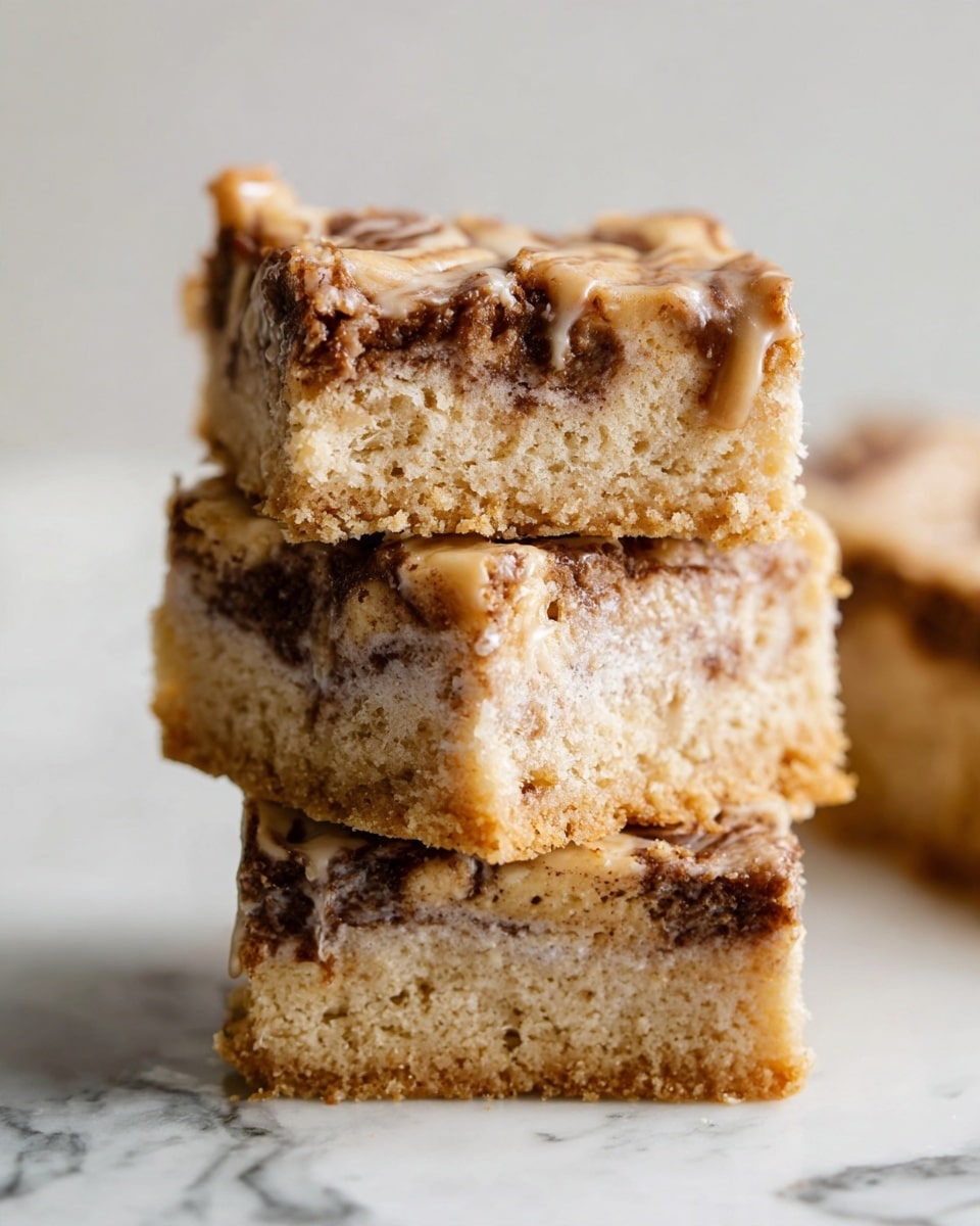 A close-up of three square bars stacked on top of each other on a white marbled surface, each bar showing two main layers: a light brown, soft, and crumbly base with a slightly porous texture, and a middle swirled layer of darker brown cream or filling mixed with a shiny glaze that looks smooth and sticky. The top bar has some dripping glaze and visible swirls of filling, adding a glossy, textured detail contrasting with the crumbly base. Soft natural light highlights the textures, giving the bars a moist and inviting look. Photo taken with an iphone --ar 4:5 --v 7