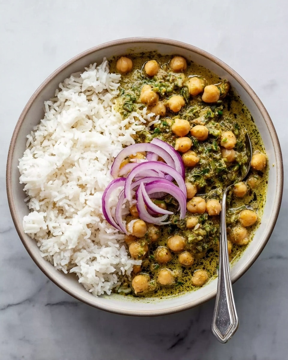 A round white bowl filled halfway with white rice showing soft, fluffy grains, and the other half filled with green chickpeas curry that has a creamy texture with some darker green patches, topped with a few thin slices of purple onion placed in the center. A silver spoon rests inside the bowl on the curry side. The bowl is set on a white marbled surface. photo taken with an iphone --ar 4:5 --v 7