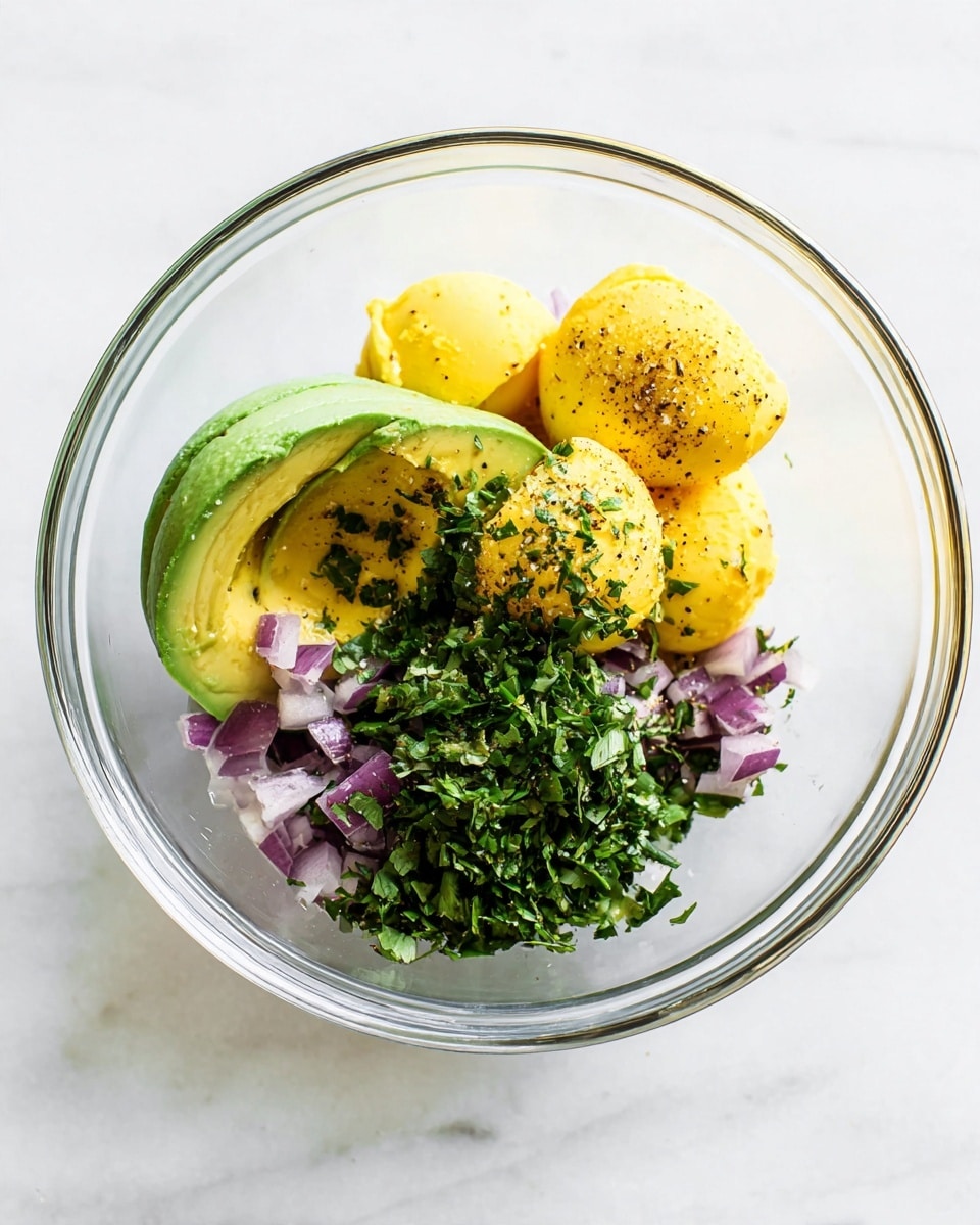 A clear glass bowl sits on a white marbled surface, containing five main layers of ingredients. On one side, there is a peeled avocado with a rough green texture and light patches. Next to it are several yellow egg yolk halves, smooth and round with black pepper specks on top. Below the yolks is a small pile of finely chopped red onion pieces, purple and white in color. Adjacent to the onion is a heap of chopped fresh green herbs with a leafy texture. The ingredients are fresh, vibrant, and neatly arranged but not mixed. Photo taken with an iphone --ar 4:5 --v 7