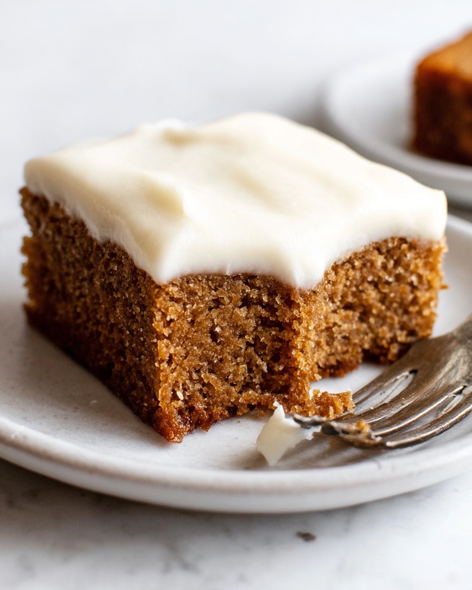 A single square piece of cake with two layers sits on a white plate over a white marbled surface. The bottom layer is thick and brown with a slightly crumbly texture, while the top layer is a smooth, creamy white frosting evenly spread. A small corner of the cake is taken off, placed near a metal fork on the right side, with a bit of frosting on the fork. The photo captures a close view, showing the details of the cake's soft inside and the frosting's smooth surface. Photo taken with an iphone --ar 4:5 --v 7