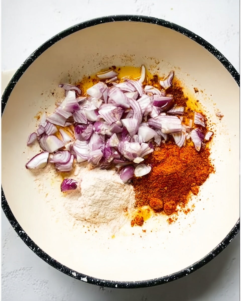 In a white pan with a black rim on a white marbled surface, small pieces of pale purple and white onions are scattered mostly on the upper half. Below them, there are two powdered spices: the left one is a soft white powder, and the right one is a bright reddish-orange powder. The spices and onions are not mixed but placed close together with some oil visible around them. photo taken with an iphone --ar 4:5 --v 7