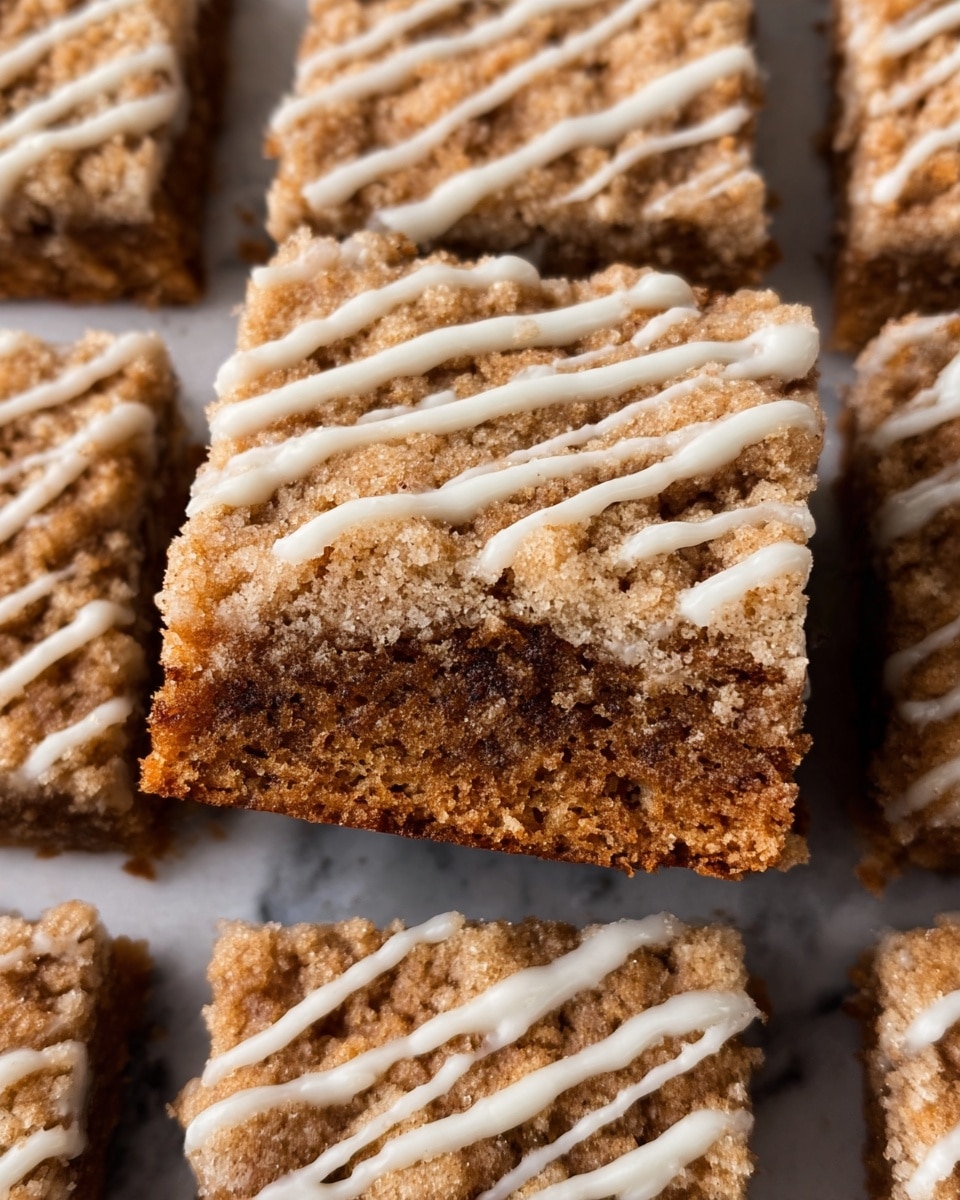 The image shows a close-up of a square piece of brown crumb cake placed on top of more crumb cake pieces, each cut into square layers. Each cake piece has two main layers: a soft, dense brown cake base with a slightly crumbly texture, and a thicker top layer of crunchy, crumbly streusel in a light golden-brown color. Thin white icing is drizzled over the entire surface in uneven, diagonal lines, adding a contrasting smooth texture to the crumbly brown top. The crumb cake pieces rest on a white marbled surface. photo taken with an iphone --ar 4:5 --v 7