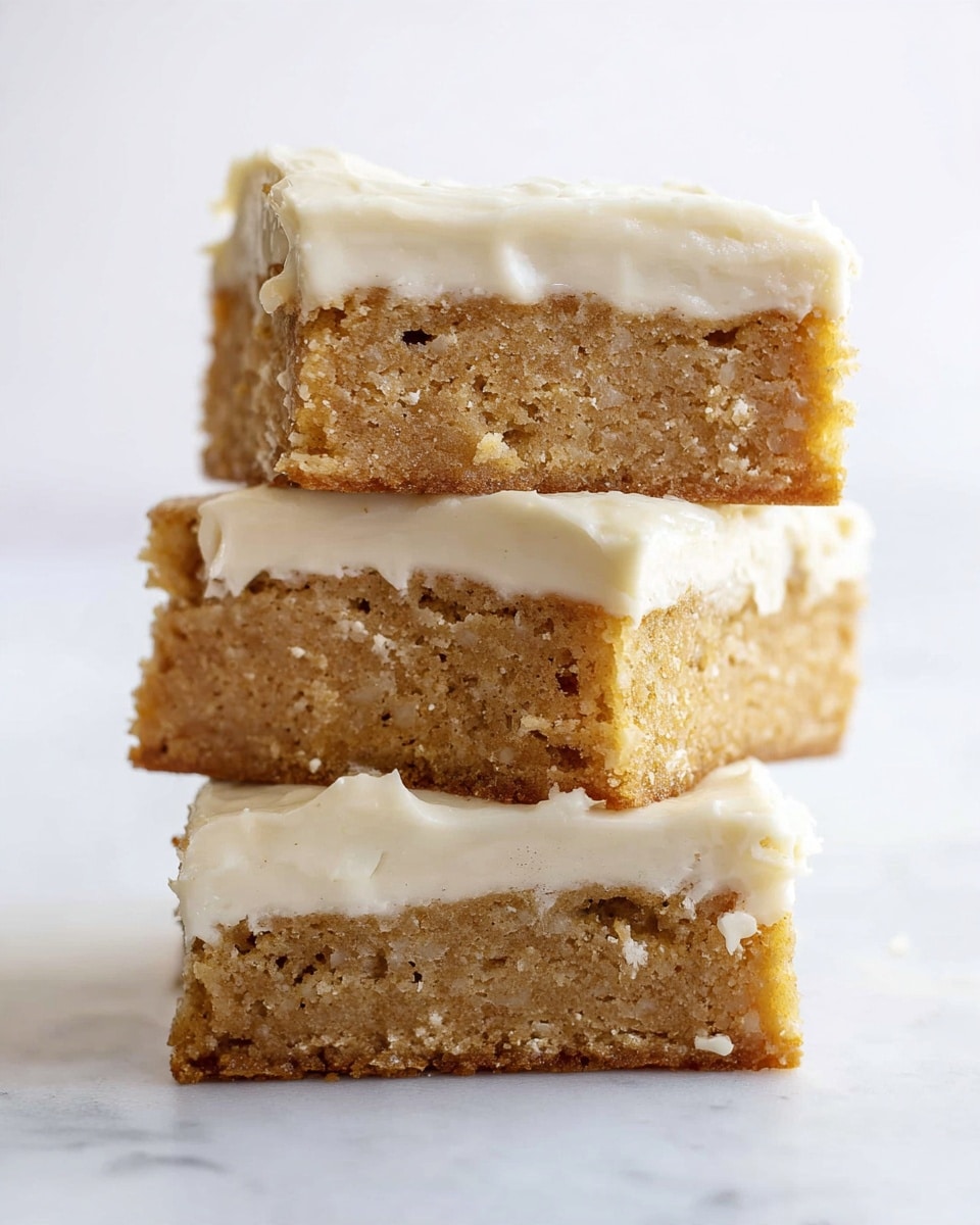A stack of three square blondies with a creamy white frosting layer between and on top of each blondie. The blondies have a golden-brown, slightly crumbly texture with visible small air pockets. The frosting is smooth and thick, evenly spread and slightly dripping at the edges. The stack is placed on a white marbled surface with a soft, bright background. Photo taken with an iphone --ar 4:5 --v 7