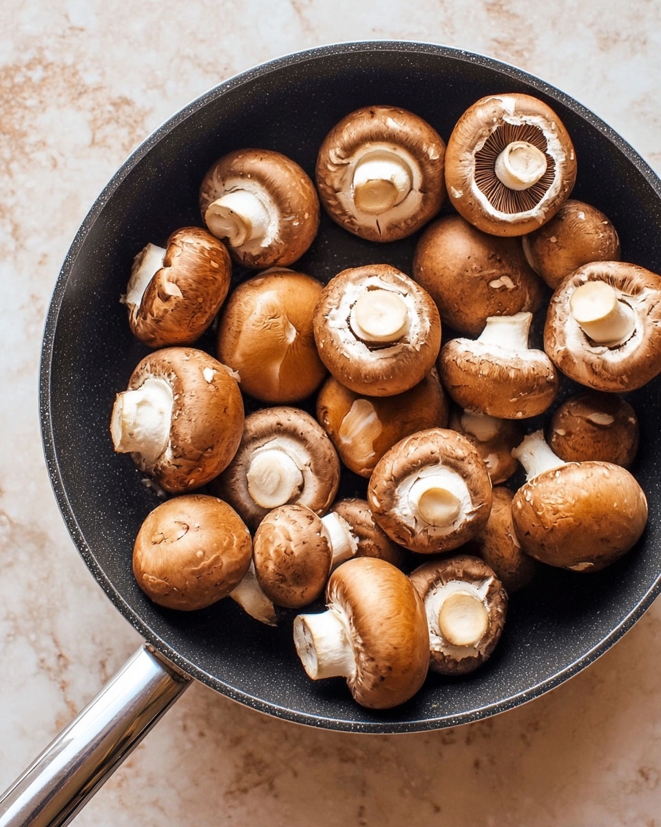 A black pan holds about twenty fresh brown mushrooms with smooth caps and white stems, some facing up showing their white, ruffled undersides with dark gills, and others lying sideways revealing round, firm caps. The pan's metal handle extends to the right, resting on a white marbled surface. The mushrooms vary in size but are mostly medium, creating a textured and natural arrangement. Photo taken with an iphone --ar 4:5 --v 7