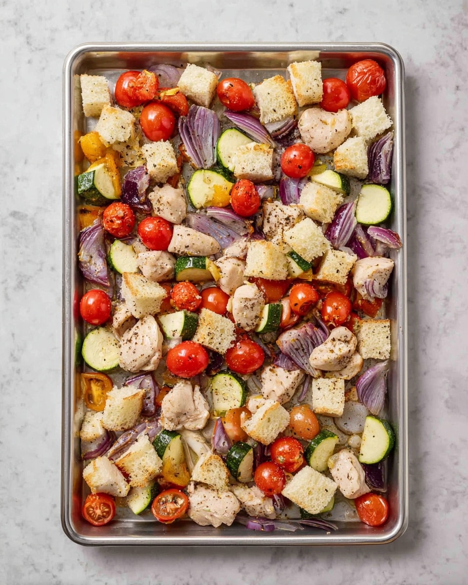 A metal baking tray holds a mix of ingredients spread across its surface, placed on a white marbled texture. The dish has four types of layers: small white and lightly browned bread cubes placed in no specific order; round bright red cherry tomatoes scattered evenly; chunks of light beige cooked chicken mixed with black pepper; thin slices of green zucchini and larger pieces of purple-red onion arranged throughout. The colors are vibrant with a mix of soft and firm textures visible. photo taken with an iphone --ar 4:5 --v 7